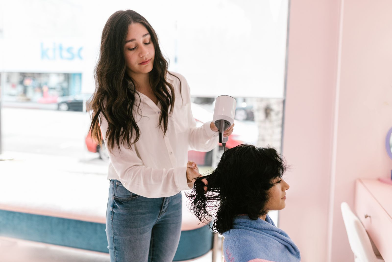 A hairstylist blow-drying a client's hair in a bright salon